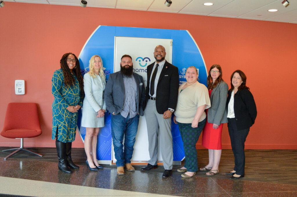 Sharnnia Artis, Liza Wilson Durant, James Villa, Omar Dennis, Joisanne Rodgers, Anne Osterman, and Rose Pascarell stand in front of a Mamata lactation pod.