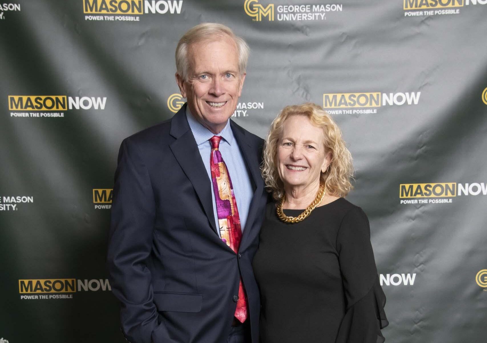 Two 2024 Winter Celebration of Giving reception attendees with Mason Now backdrop.
