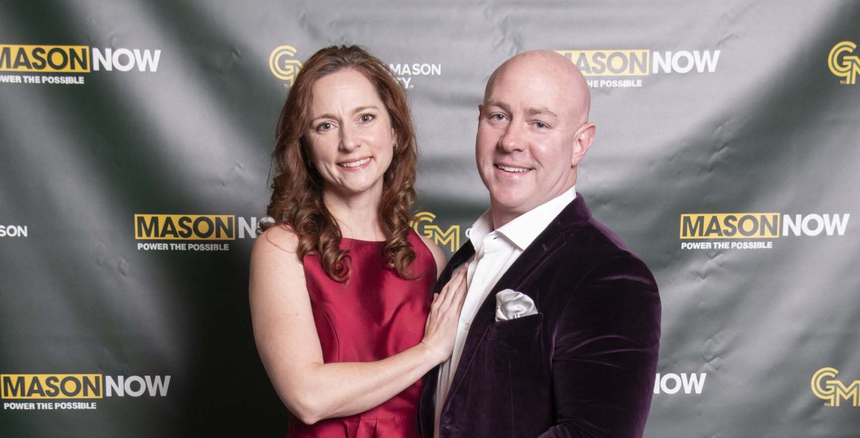 Two 2024 Winter Celebration of Giving reception attendees with Mason Now backdrop.