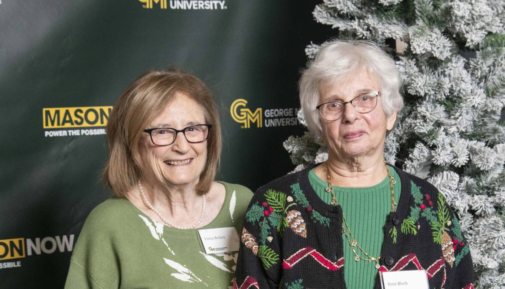 Two 2024 Winter Celebration of Giving reception attendees with Mason Now backdrop.