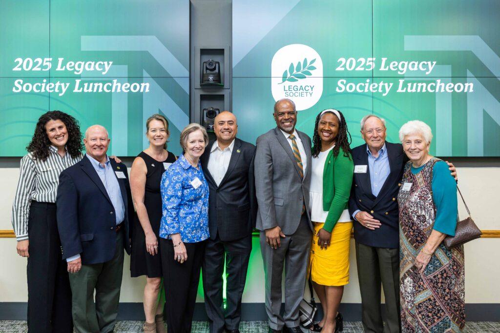 Legacy Society Luncheon attendees stand side by side in front of a wall.