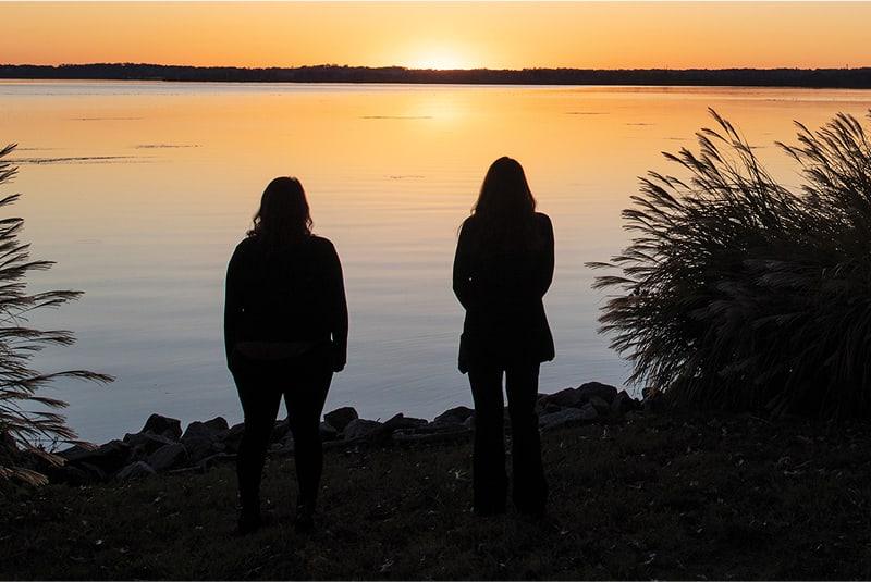 Two students looking at a lake at sunset