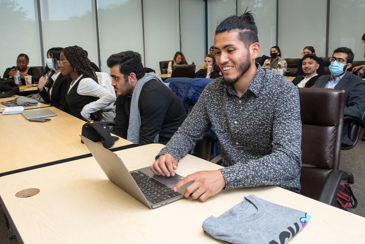 Smiling male student seated and using his laptop