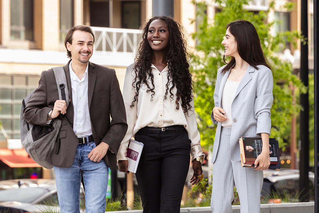Three students dressed in business attire and walking together outside