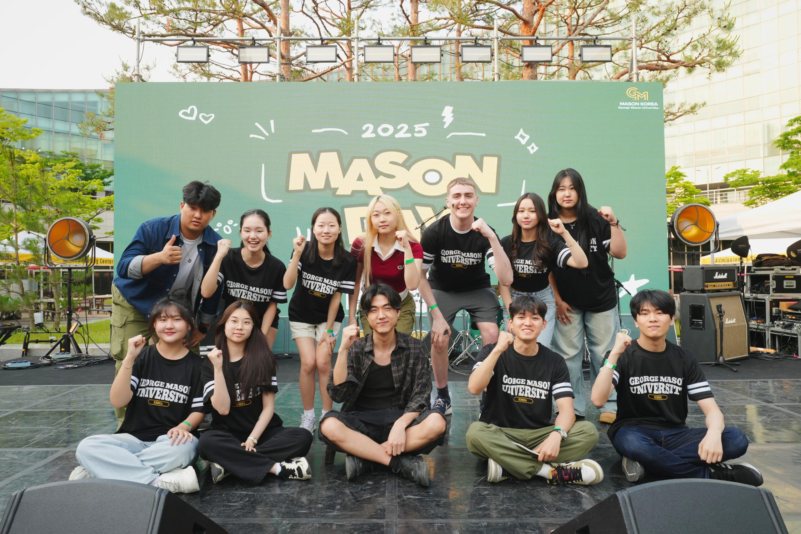 A group of students on the a stage with a green backdrop sign that says Mason Korea