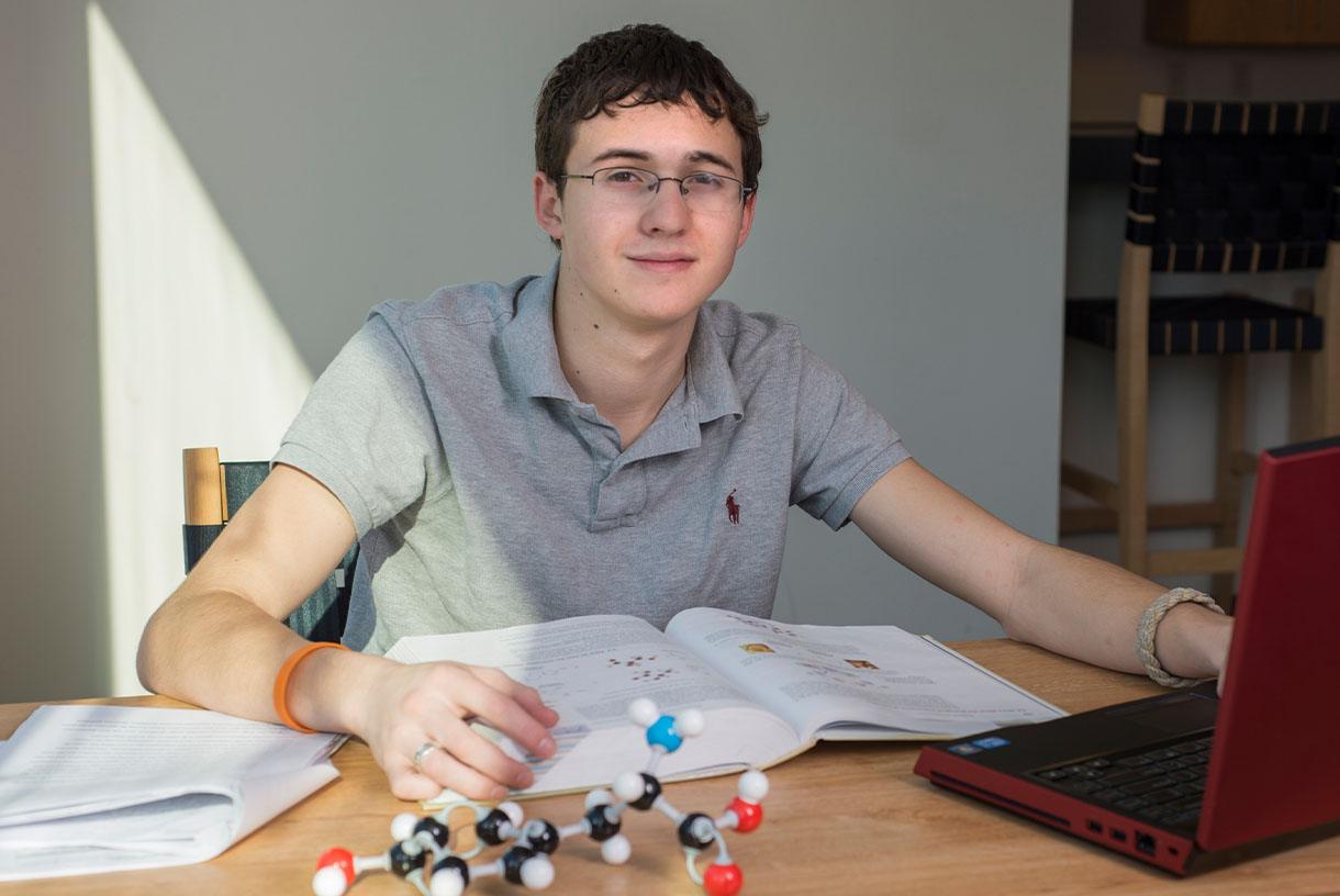 Smiling student sitting at a table with a notebook and DNA model