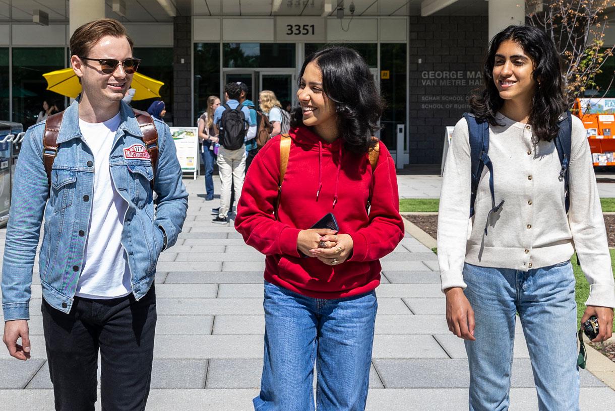 Three smiling students walking together outside