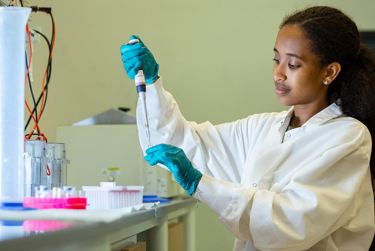 Student wearing a lab coat and working on DNA