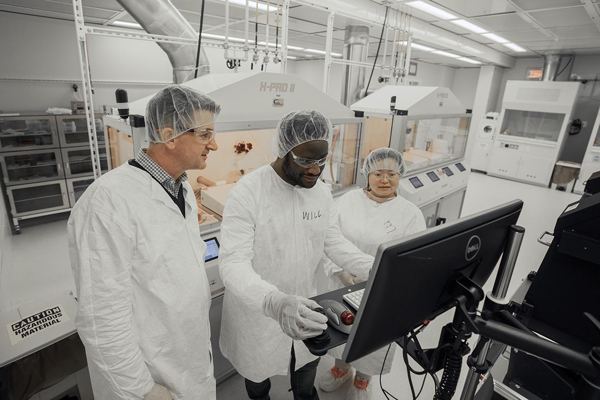 Three people wearing lab coats and hair nets in a laboratory