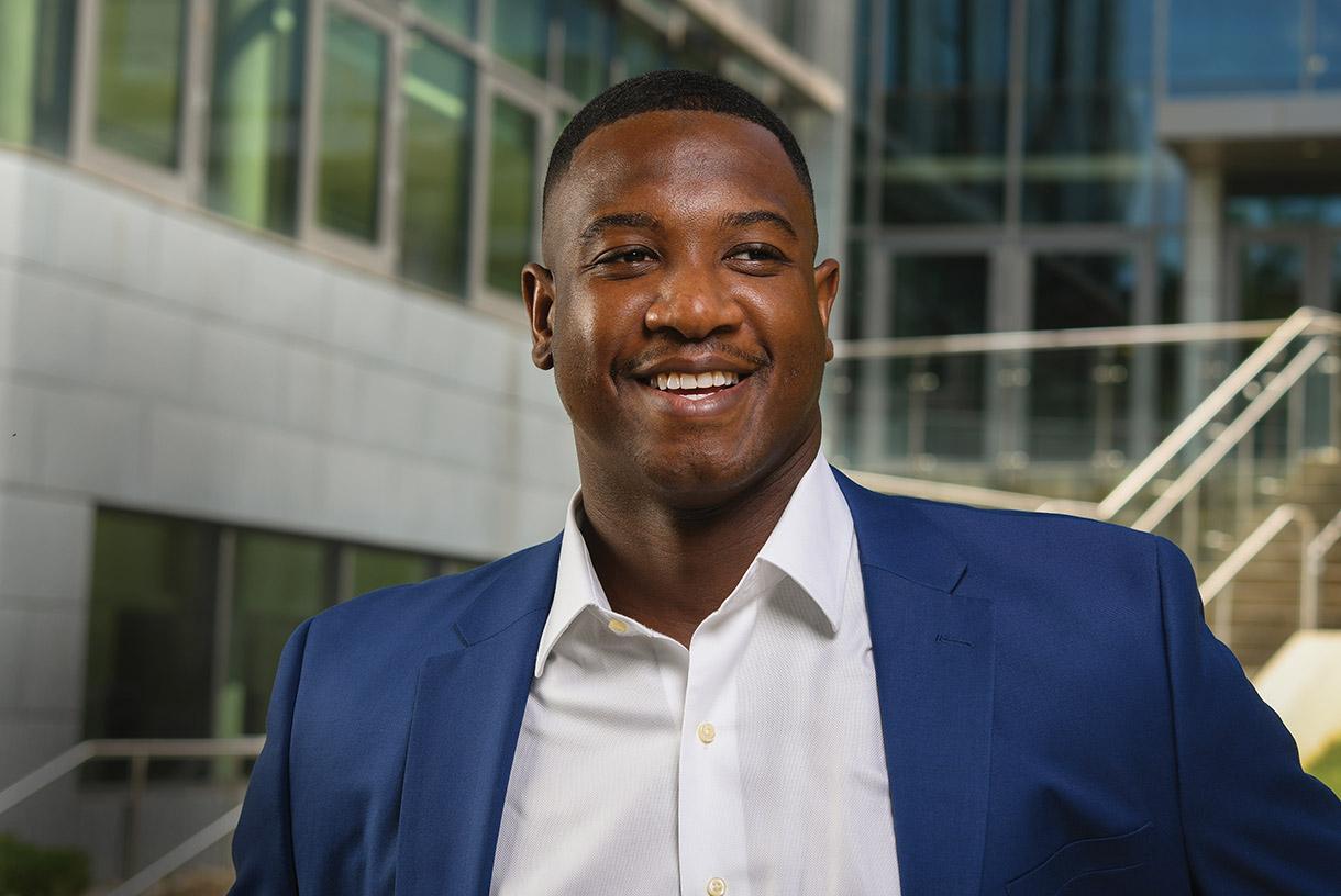 A smiling man wearing a blue blazer and white button down shirt