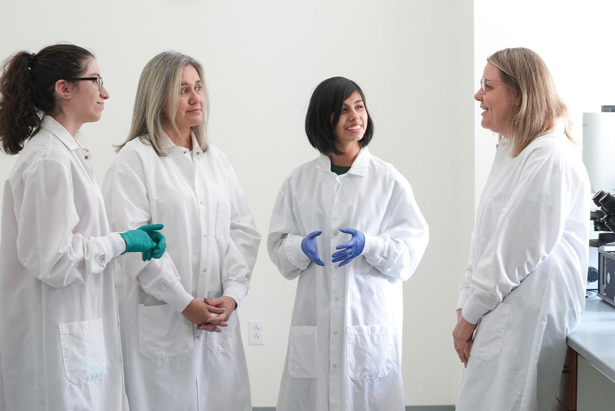Four people wearing lab coats and protective gloves