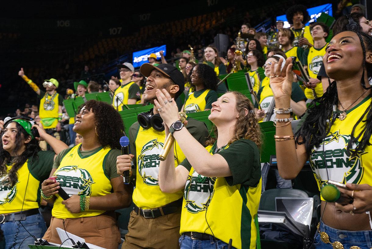Students wearing matching green and yellow t-shirts and cheering in a stadium
