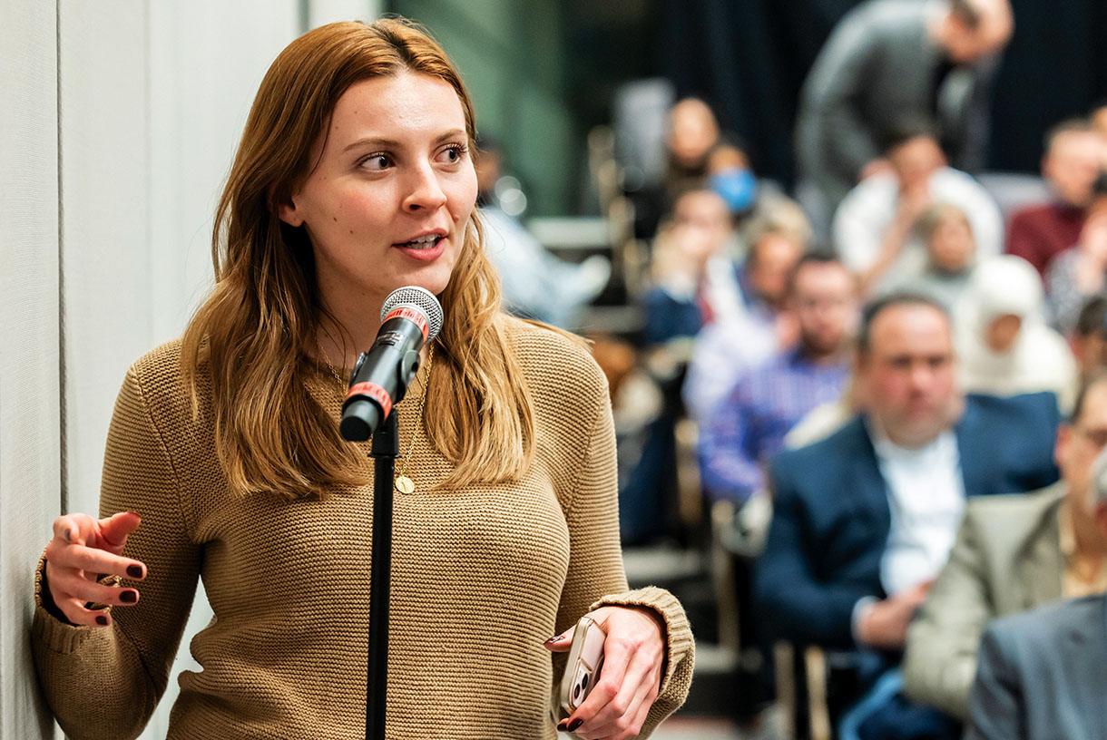 Woman standing and speaking into microphone in front of an audience