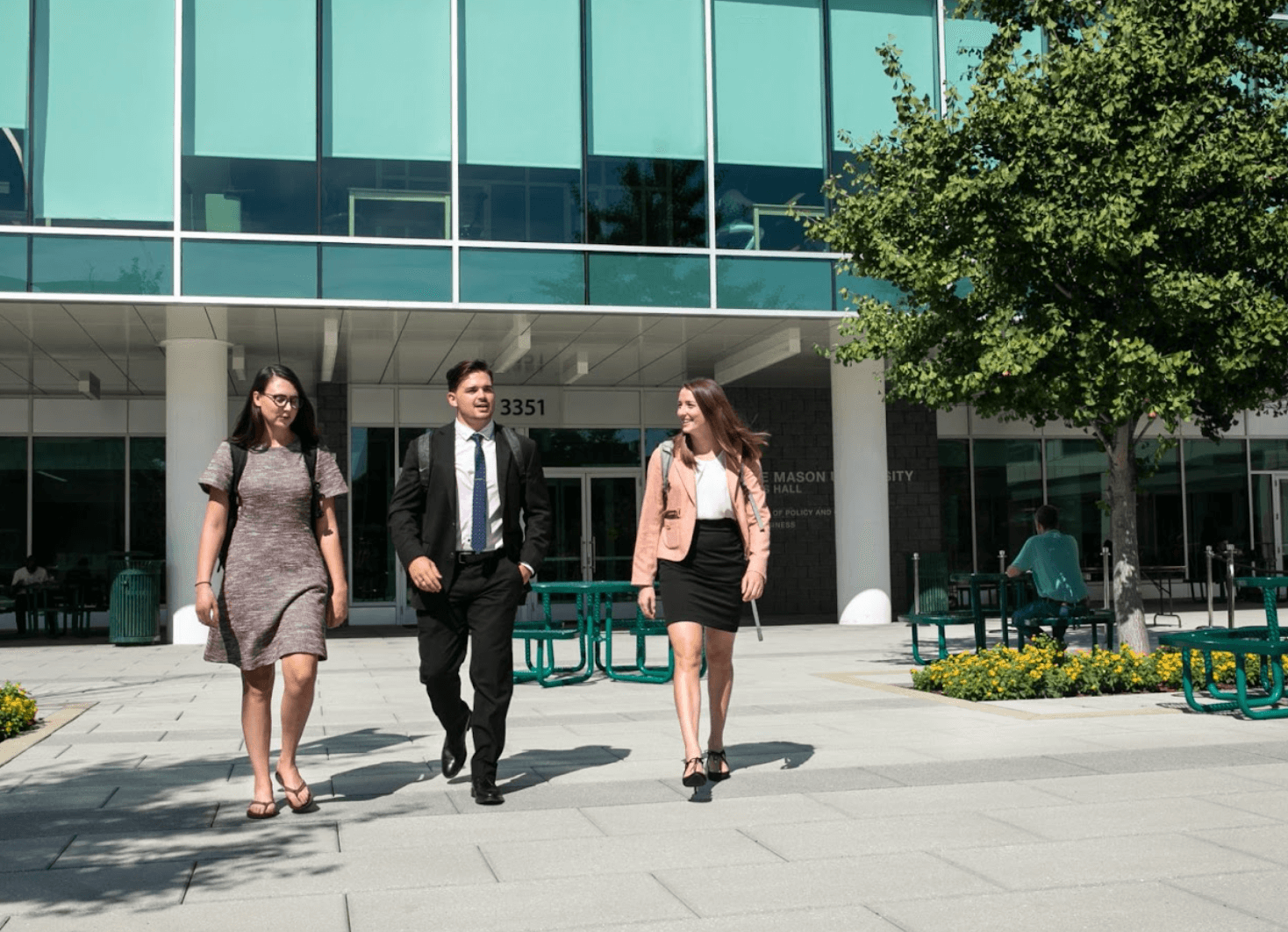 Three people in business casual and walking outside a glass building