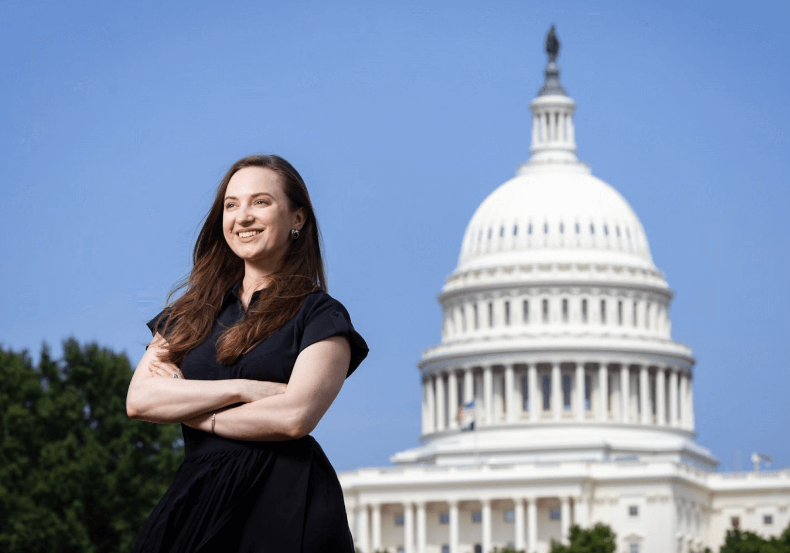 Woman wearing a black dress and posing with her arms crossed in front of the U.S. Capitol building