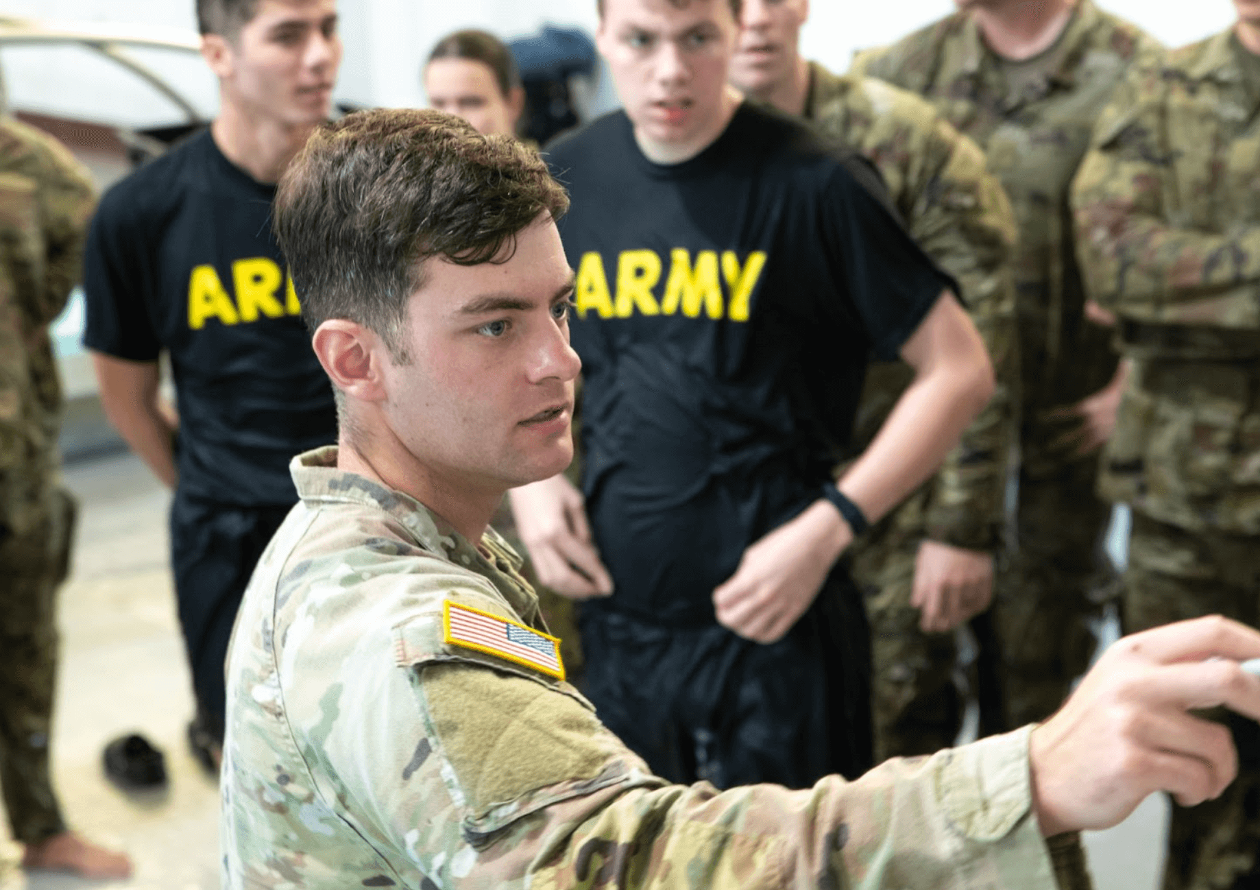Man wearing his military uniform and writing on a wall with Army soldiers behind him