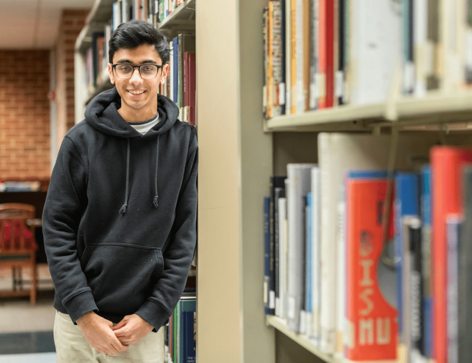 Smiling student leaning on library bookshelves
