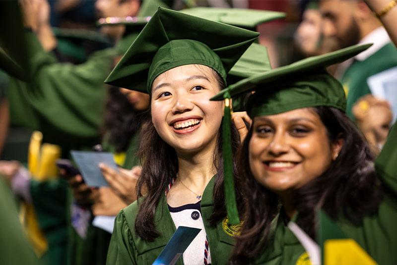 Close up of a smiling graduate wearing her green cap and gown