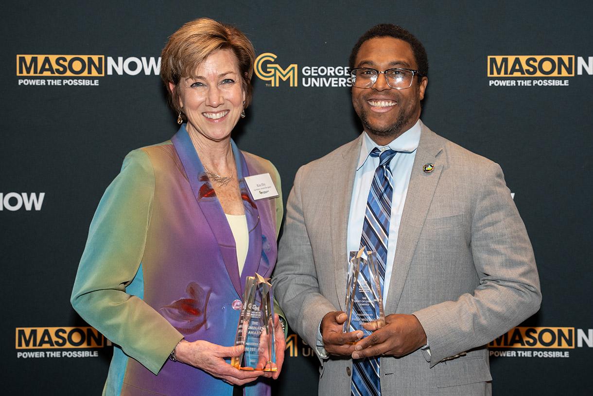 Woman wearing a colorful blazer holds award next to man in tan blazer