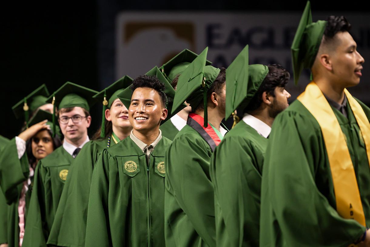 Smiling graduates wearing their green commencement gowns and hats