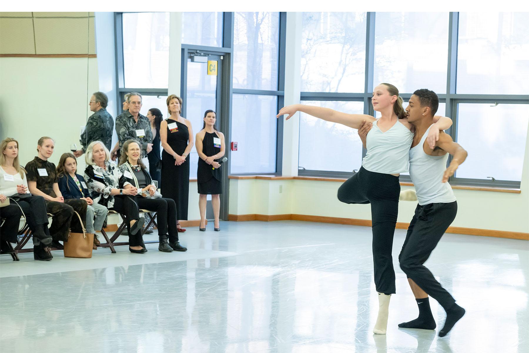 Two dancers perform in a dance studio as the audience watches.