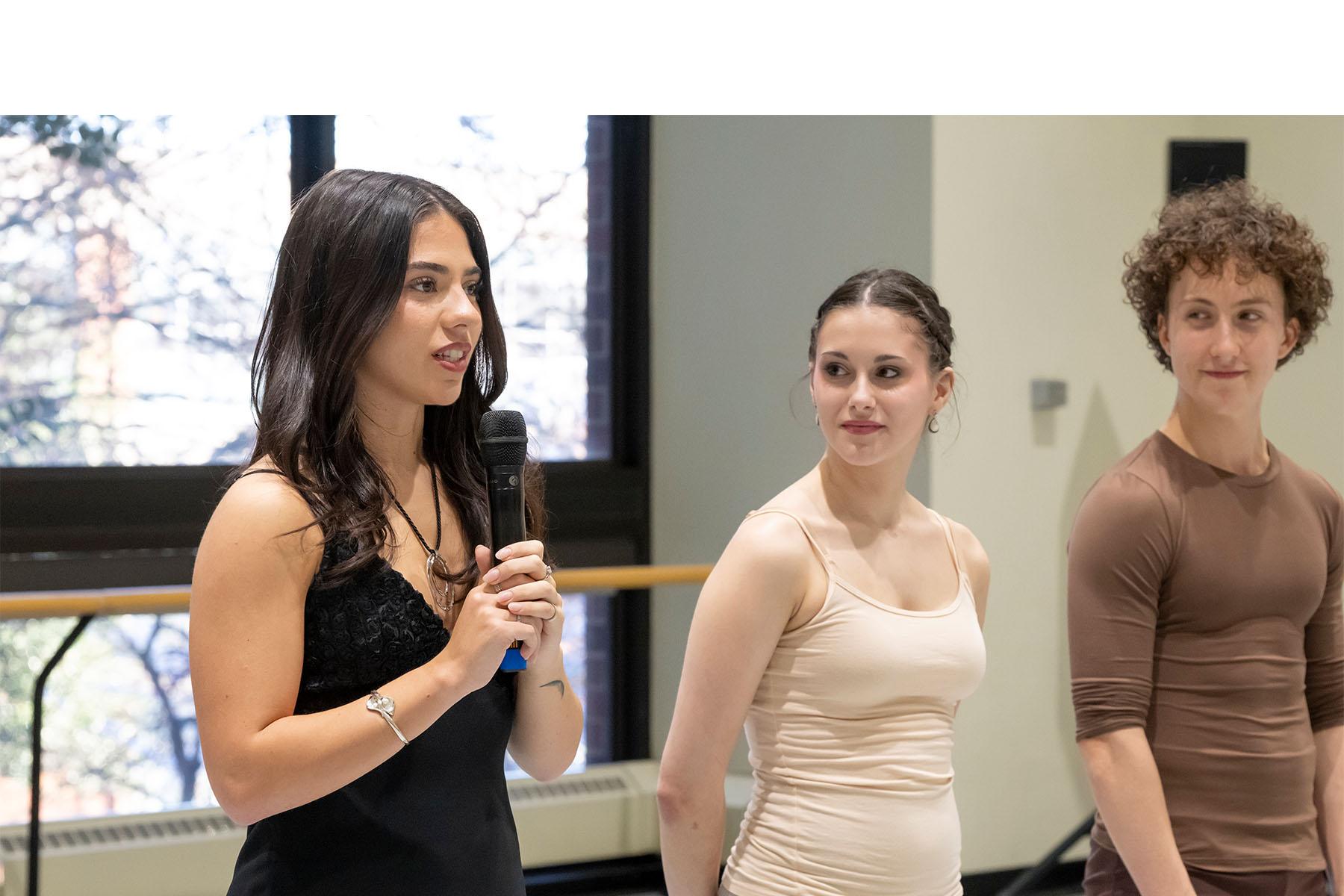 A speaker stands in a dance studio with two dancers beside them.