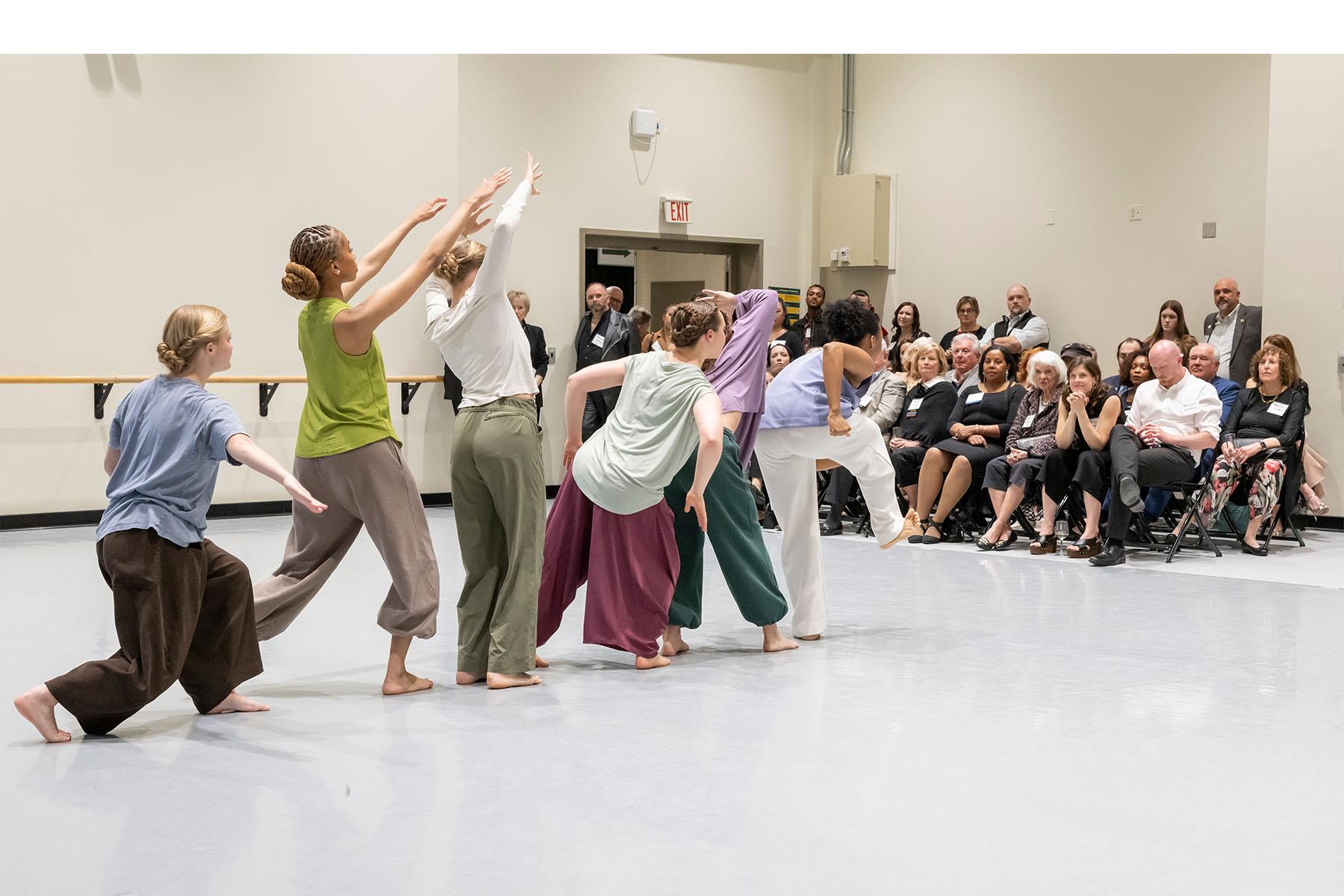 Six dancers perform in a dance studio as the audience watches.