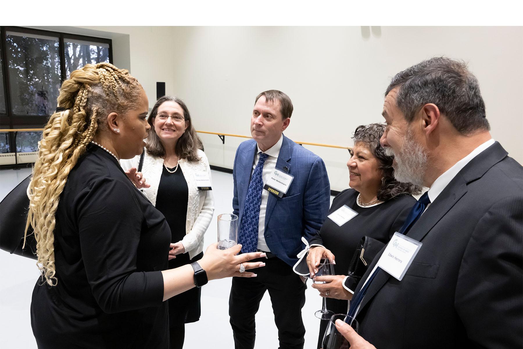 Five event attendees speaking with each other.