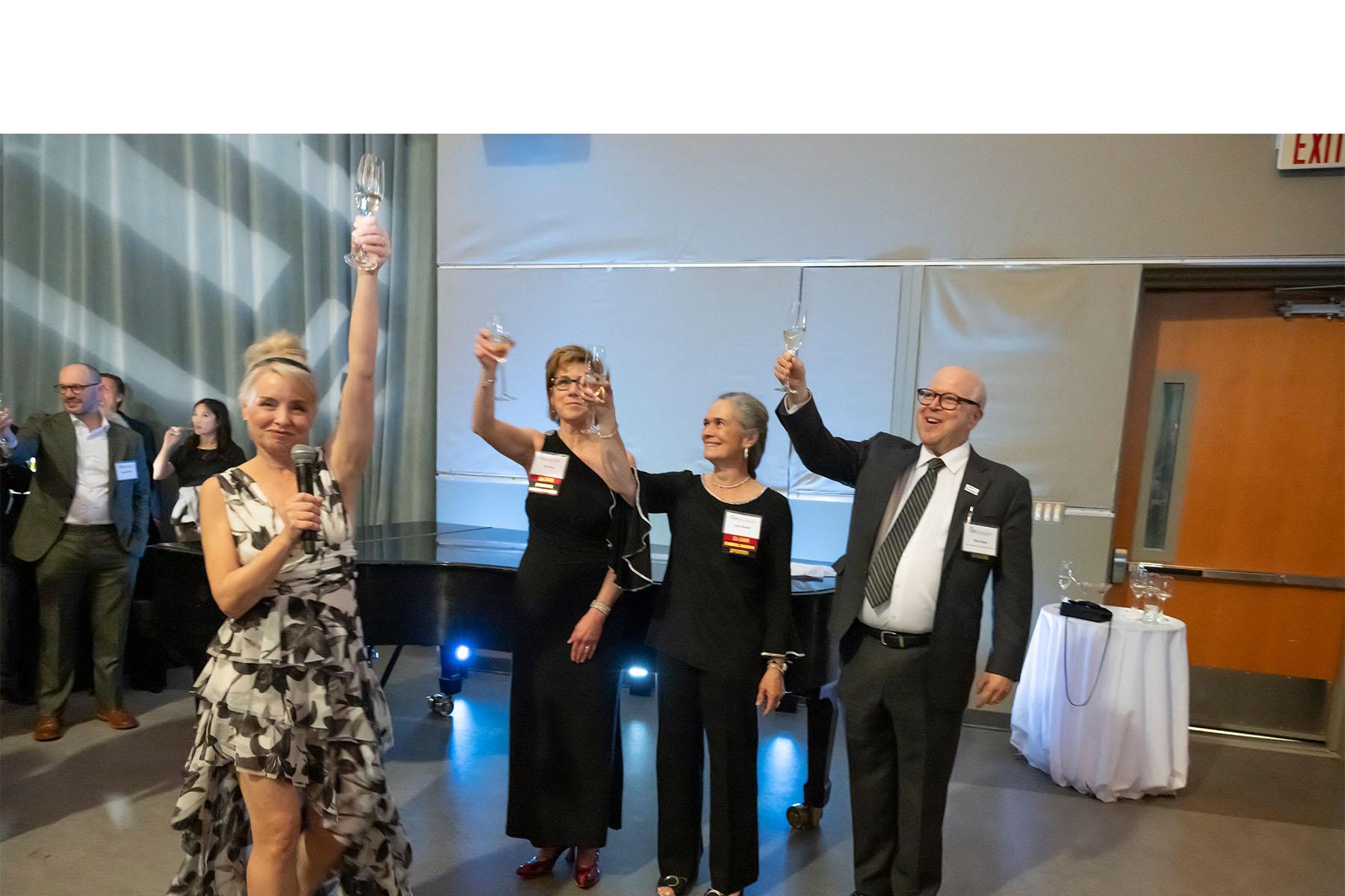 Four event speakers raise their drink glasses in a toast.