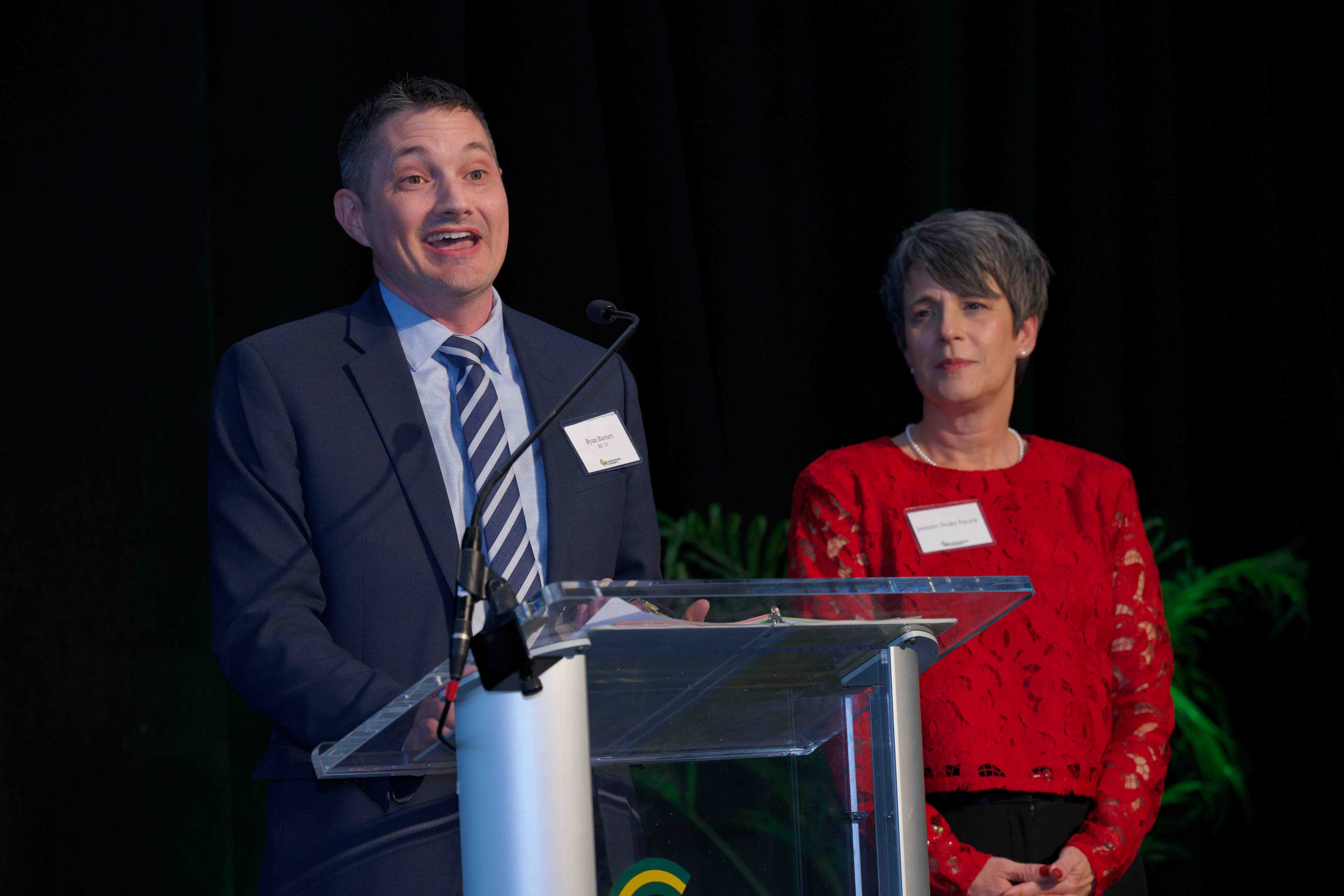Ryan Barnett and Jennifer Drake Patrick stand at podium at Celebrating Our Champions event.