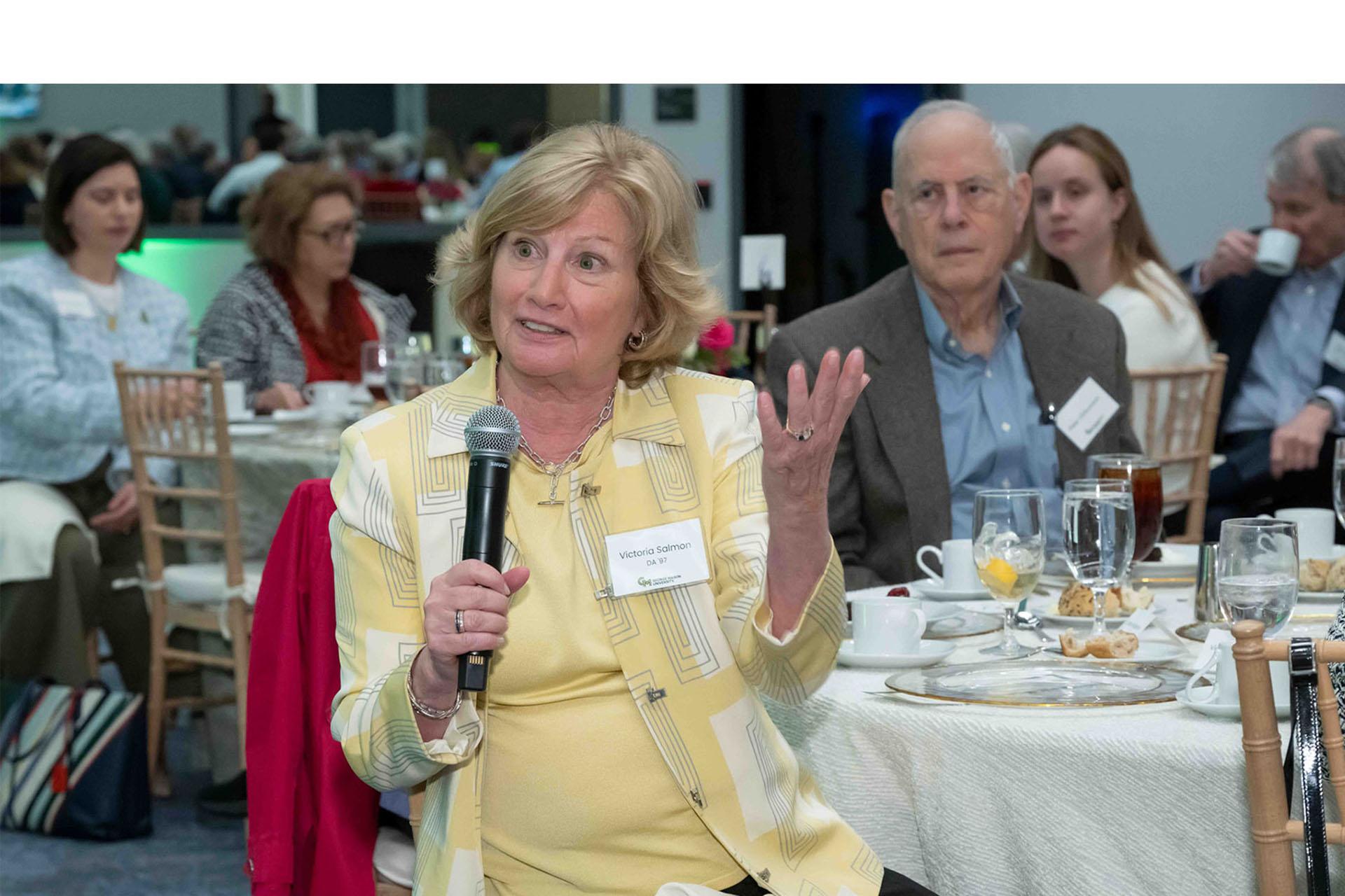 Event attendee holding microphone while seated at a table.