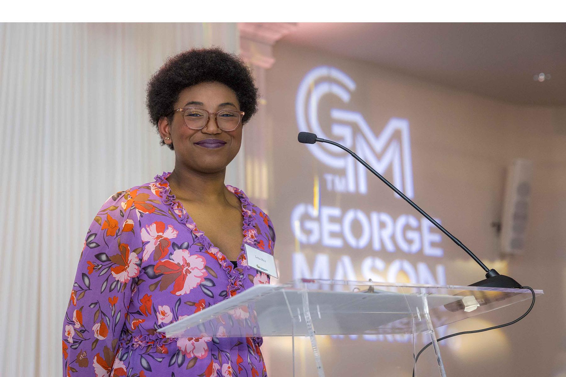 Lena Rice stands at speaker podium with the George Mason logo in the background.