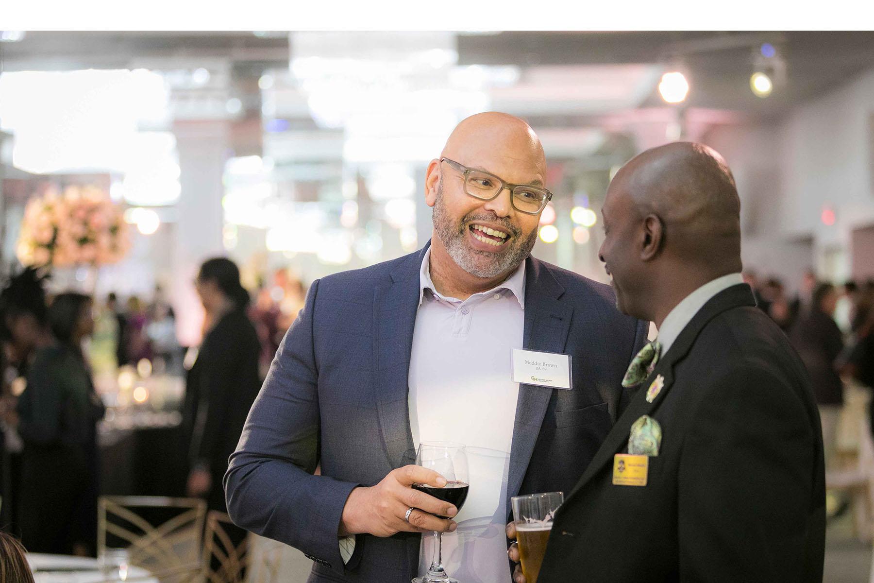 Two event attendees talking together in the reception area while holding drinks.