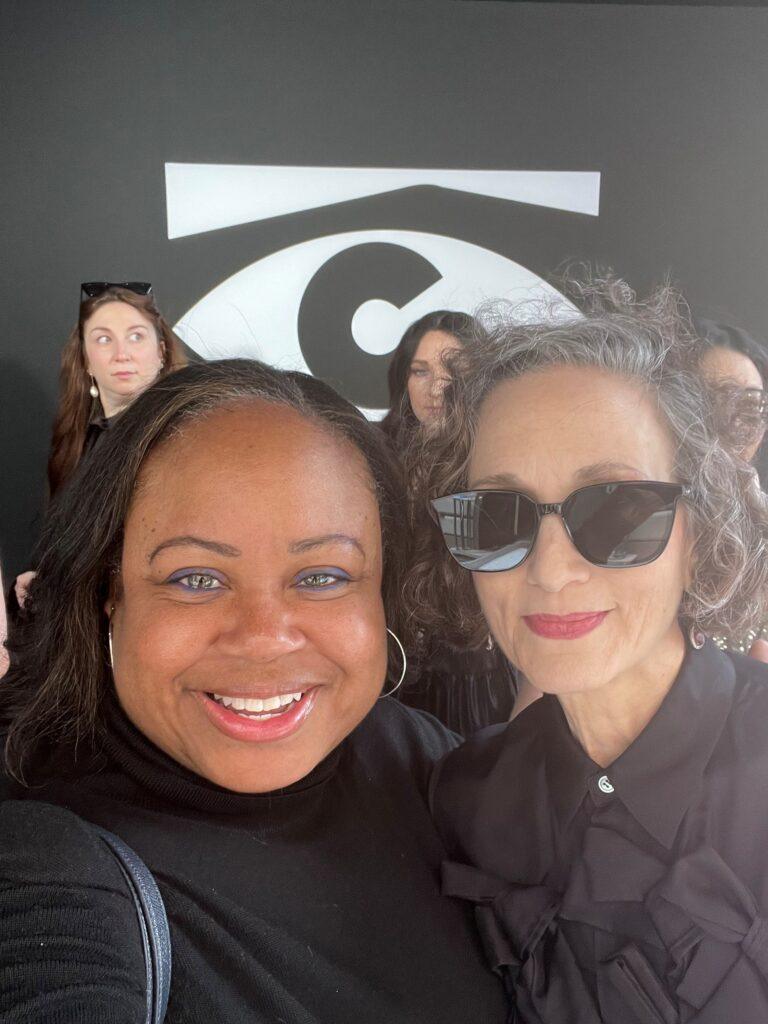 Gilda Squire and Bebe Neuwirth pose for a close-up selfie with a backdrop behind them.