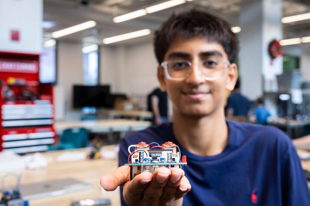 Student in a robotics lab holding a robotics piece with an outstretched hand. 